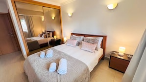 A hotel room with a large bed, a mirror, and a bedside table with a lamp. - MAR SOL Villa in Vilamoura (Loulé)