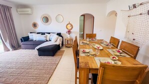 A modern living room with a sofa, a dining table set for four, and a small side table with a vase. - MAR SOL Villa in Vilamoura (Loulé)