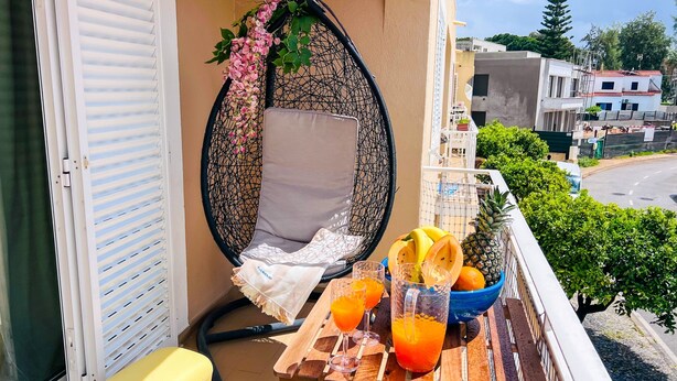 A balcony with a cushioned seating area, a bowl of fruit, and glasses of orange juice. - MAR SOL Villa in Vilamoura (Loulé)