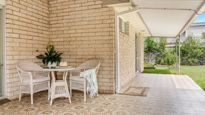 Eine überdachte Terrasse mit Korbmöbeln, einem Blumentopf und einem gemusterten Boden.