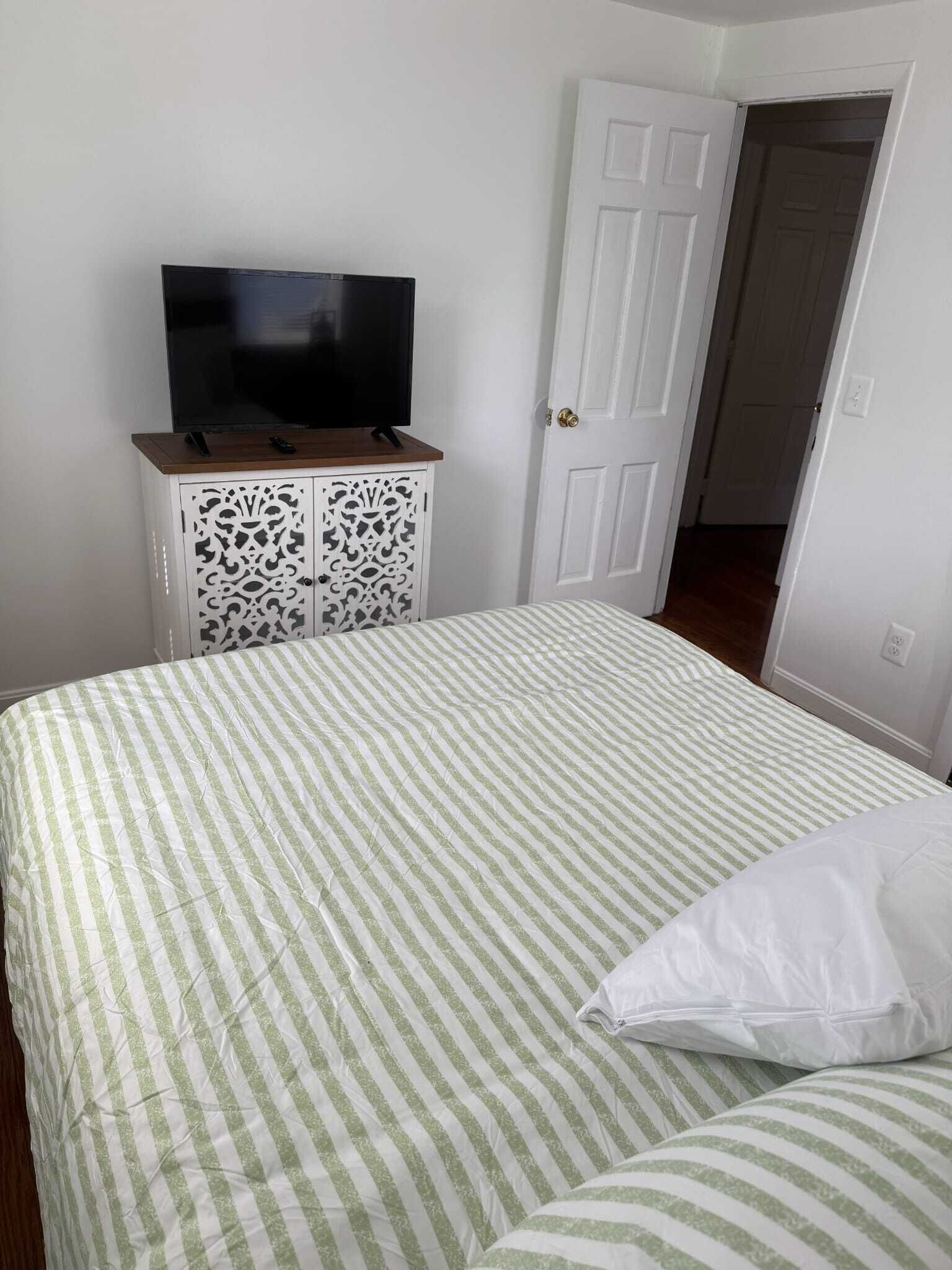 A room with a bed, a TV on a cabinet, and a door.