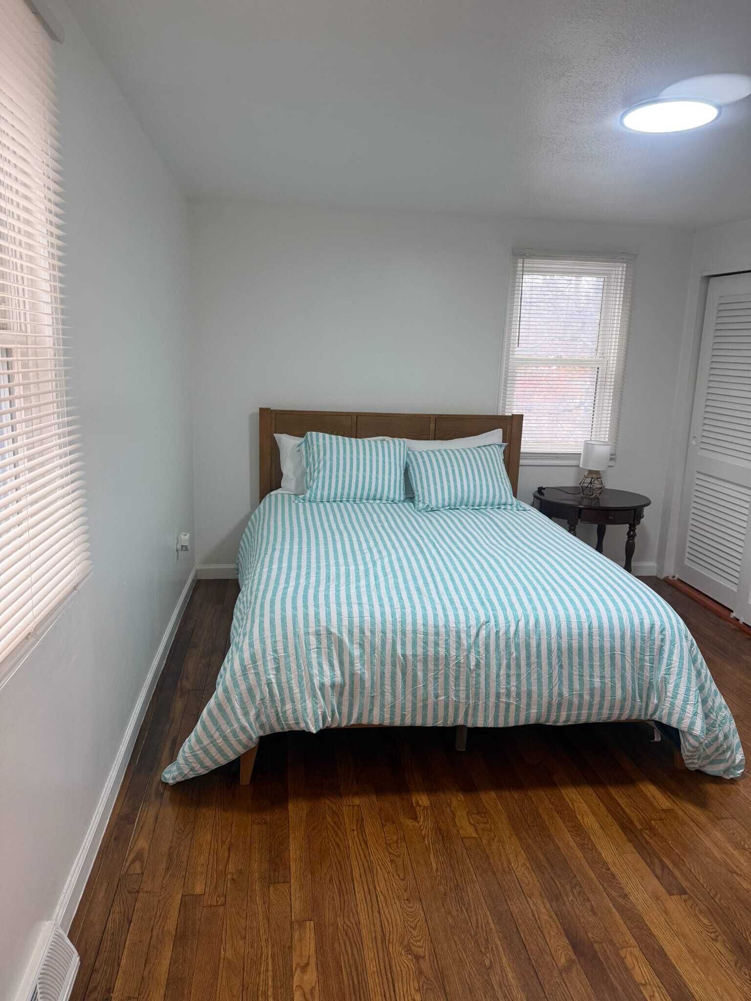 Une chambre à coucher avec un lit en bois, des murs blancs et une fenêtre avec des stores.