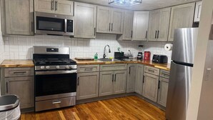 Una cocina con armarios grises, un refrigerador de acero inoxidable, un microondas, una estufa y un lavamanos.