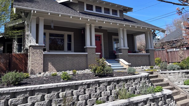 A two-story house with a porch, a red door, and a brick foundation. - UPS Neighborhood Apartment (Tacoma)