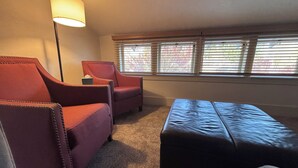 A room with a sofa, armchair, ottoman, and a lamp. - UPS Neighborhood Apartment (Tacoma)