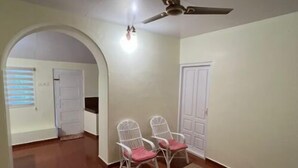A spacious room with a tiled floor, two white chairs with red cushions, a small table, and a ceiling fan. - Eco-Friendly Plantation Retreat Near Thekkady (Anakkara)