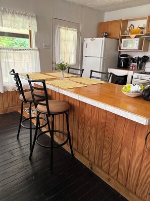 A kitchen with a wooden island, black chairs, a white refrigerator, and a microwave on a wooden countertop. - Charming 2-bedroom bungalow with AC, WiFi,washer and dryer, ON THE CREEK. (Ellwood City)