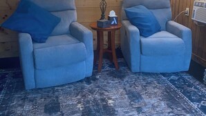 A room with two grey armchairs, a wooden headboard, a bear picture, a lamp, and a floor lamp.