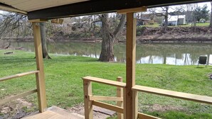 A wooden deck with a railing overlooking a pond and a grassy area with trees.