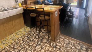 A kitchen with a wooden island, bar stools, a ceiling fan, and a fireplace.