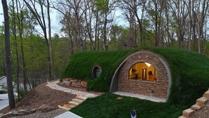 Une maison avec un toit recouvert d’herbe et des murs en pierre, entourée d’une pelouse bien entretenue et d’un chemin de pierre menant à l’entrée.