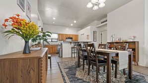A modern kitchen with wooden cabinets, a dining area with dark chairs, and a decorative vase with flowers on the counter. - Cozy/Relaxing Home in Sierra Vista (Sierra Vista)