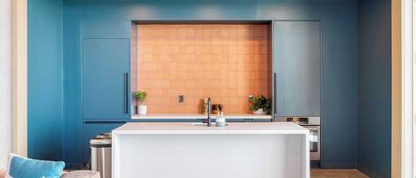 A modern kitchen with a central island, blue walls, and a wooden backsplash.
