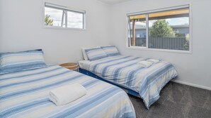 A bedroom with two beds, a small side table, and two windows.