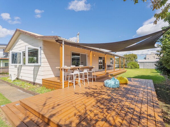 Una casa de un piso con terraza de madera, un porche cubierto y un ventanal grande.