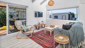 A modern living room with a large window, a ceiling fan, a TV, and a colorful rug.