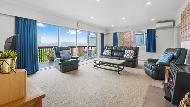 A spacious living room with a large sliding glass door leading to a balcony, a fireplace, and a clock on the wall.