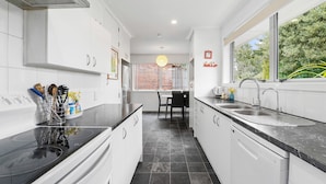 A modern kitchen with white cabinets, a black countertop, a built-in dishwasher, and a window providing a view of greenery outside.