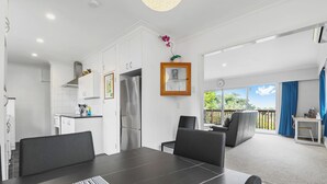 A modern kitchen with white cabinets, a stainless steel refrigerator, and a dining area with a dark table and chairs.