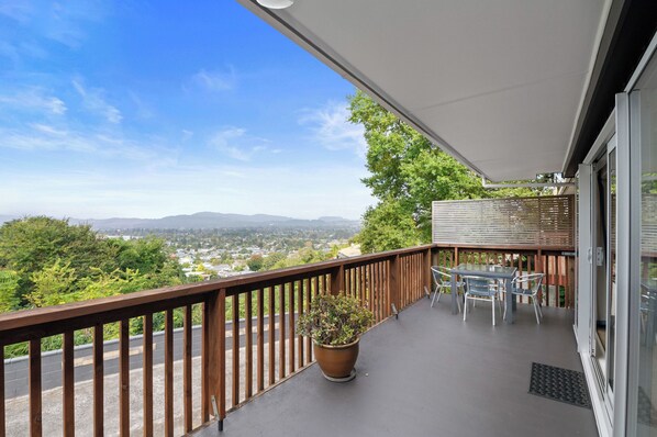 A balcony with a view of a cityscape, a potted plant, and a table with chairs.