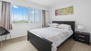 A bedroom with a large bed, a nightstand, a chair, and a window with curtains.