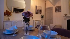 A dining table set with plates, glasses, and a vase with a single flower.