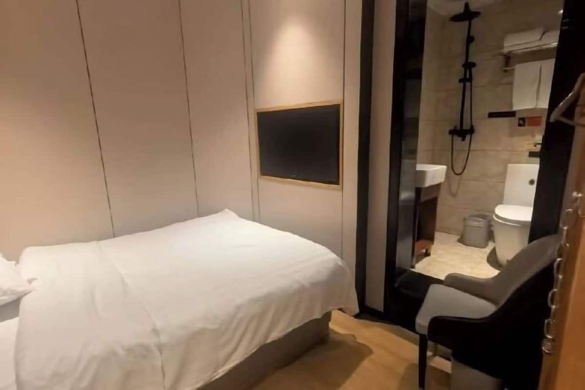A bedroom with a bed, a chair, and a shower area.