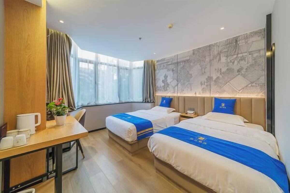 A hotel room with two beds, a desk, a chair, a window with curtains, and a wall with a map.