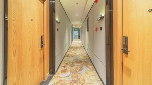 A hotel corridor with wooden doors, a patterned carpet, and a ceiling with recessed lighting.