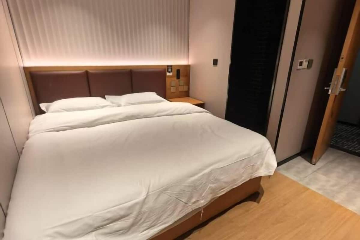 A neatly made bed with white linens, a wooden headboard, and a bedside table with a lamp.