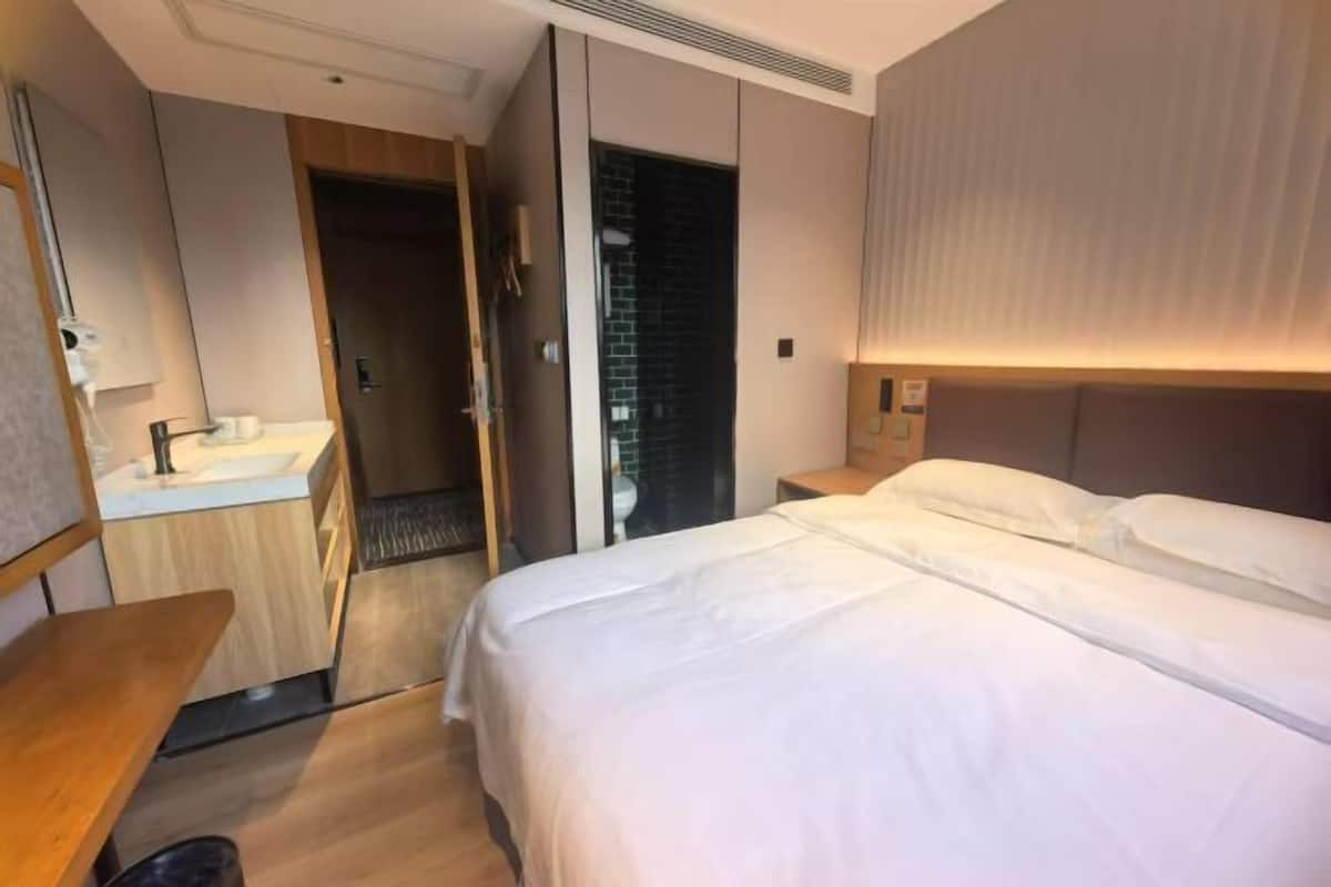 A hotel room with a bed, a bedside table, a mirror, a sink, and a wardrobe.