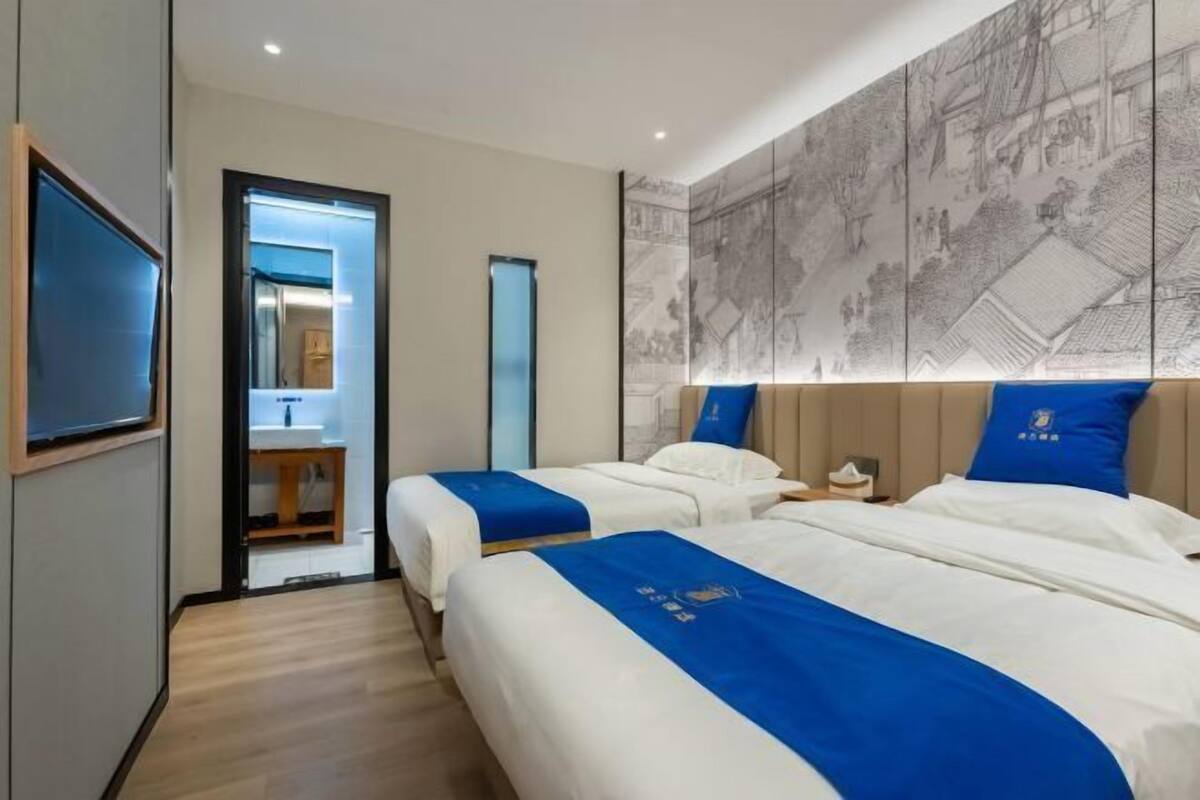 A hotel room with two beds, a large wall mural, and a bathroom visible through an open door.