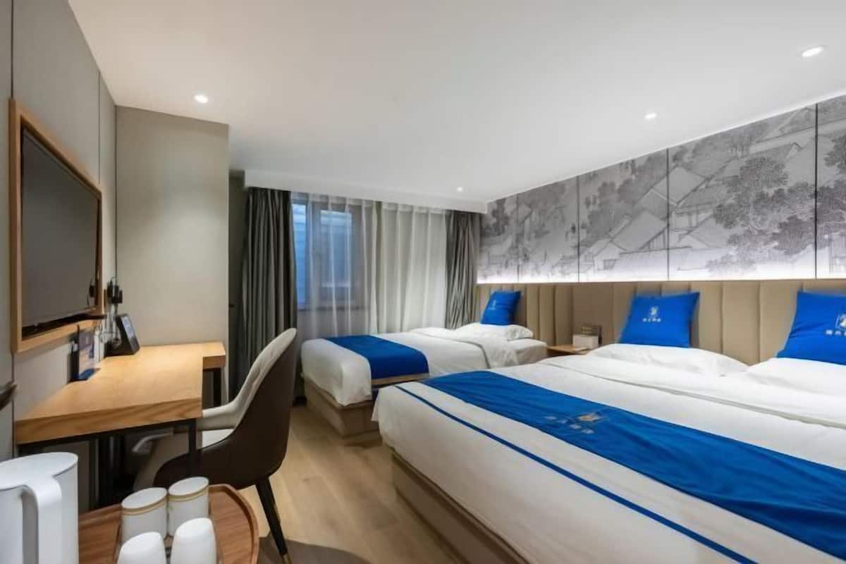 A hotel room with two beds, a desk, a chair, a TV, and a large window with curtains.