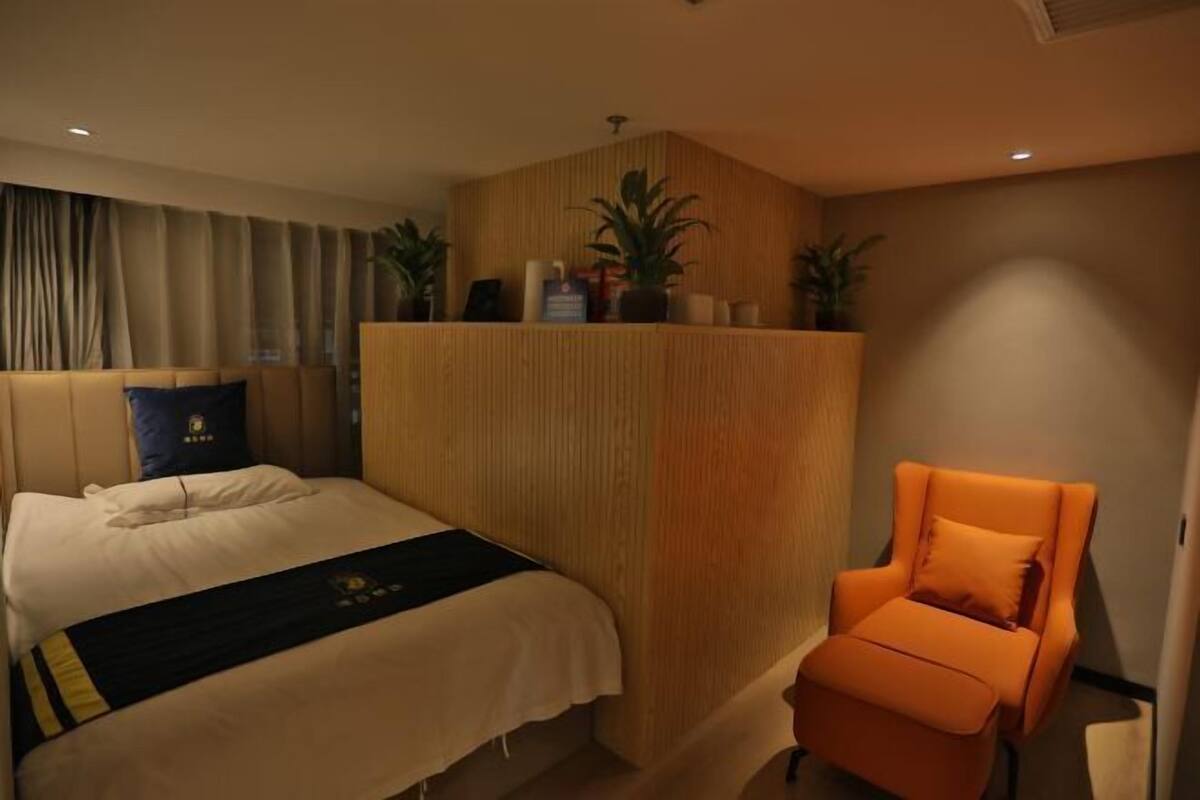 A hotel room with a bed, a wooden headboard, a seating area, and a potted plant.