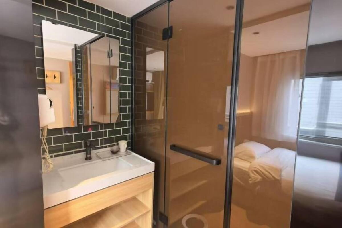 A modern bathroom with a glass shower enclosure, a white sink, and a mirror with a green-tiled backsplash.