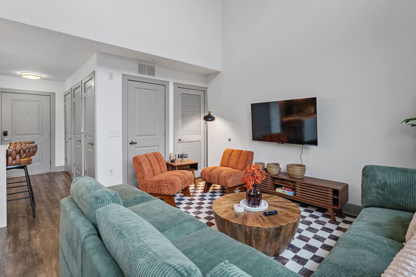 A living room with a large TV, two orange armchairs, a green sofa, and a wooden coffee table.