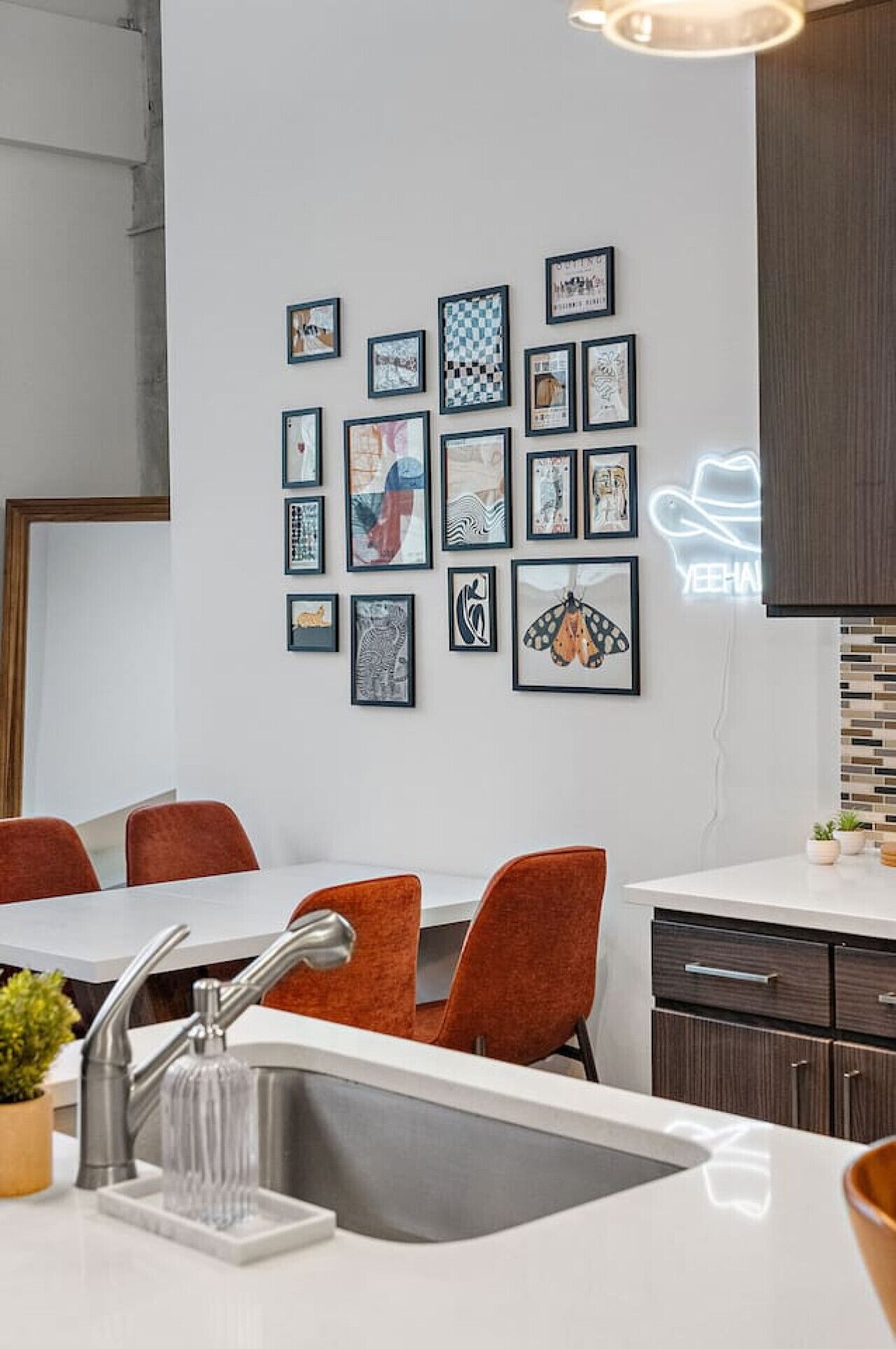 A modern kitchen with a white countertop, a stainless steel sink, and a neon sign.