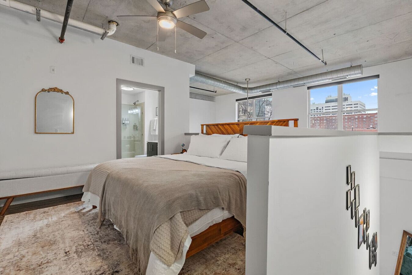 Een slaapkamer met een bed, een spiegel, een plafondventilator en uitzicht op de stad door een raam.