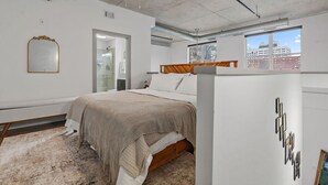 A bedroom with a bed, a mirror, a ceiling fan, and a view of the city through a window.