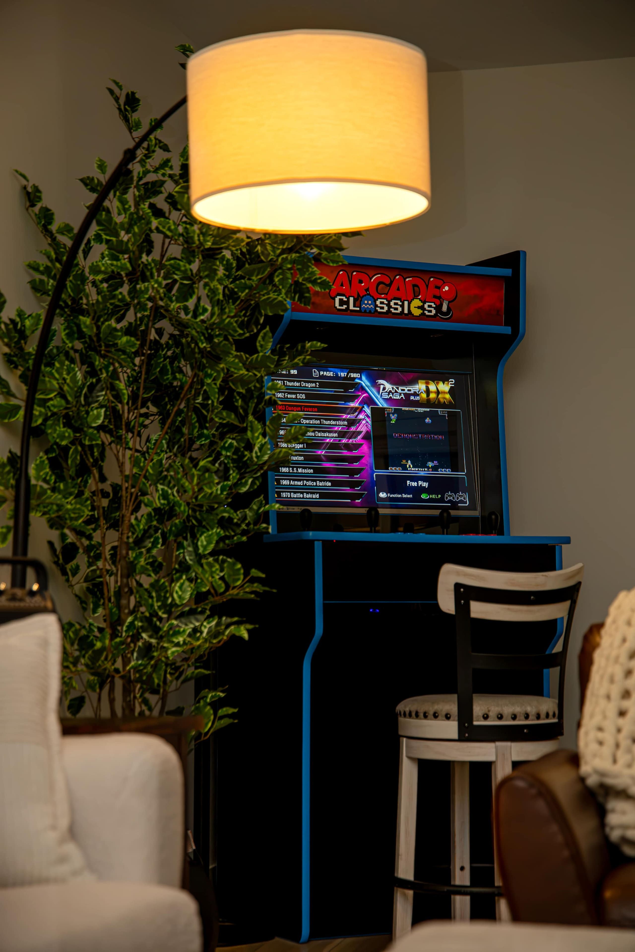 A retro gaming console with a selection of classic games displayed on its screen, set against a backdrop of a potted plant and a chair.