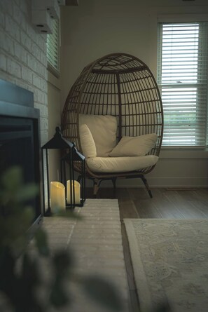 A room with a wicker chair, a fireplace, and a window with blinds.