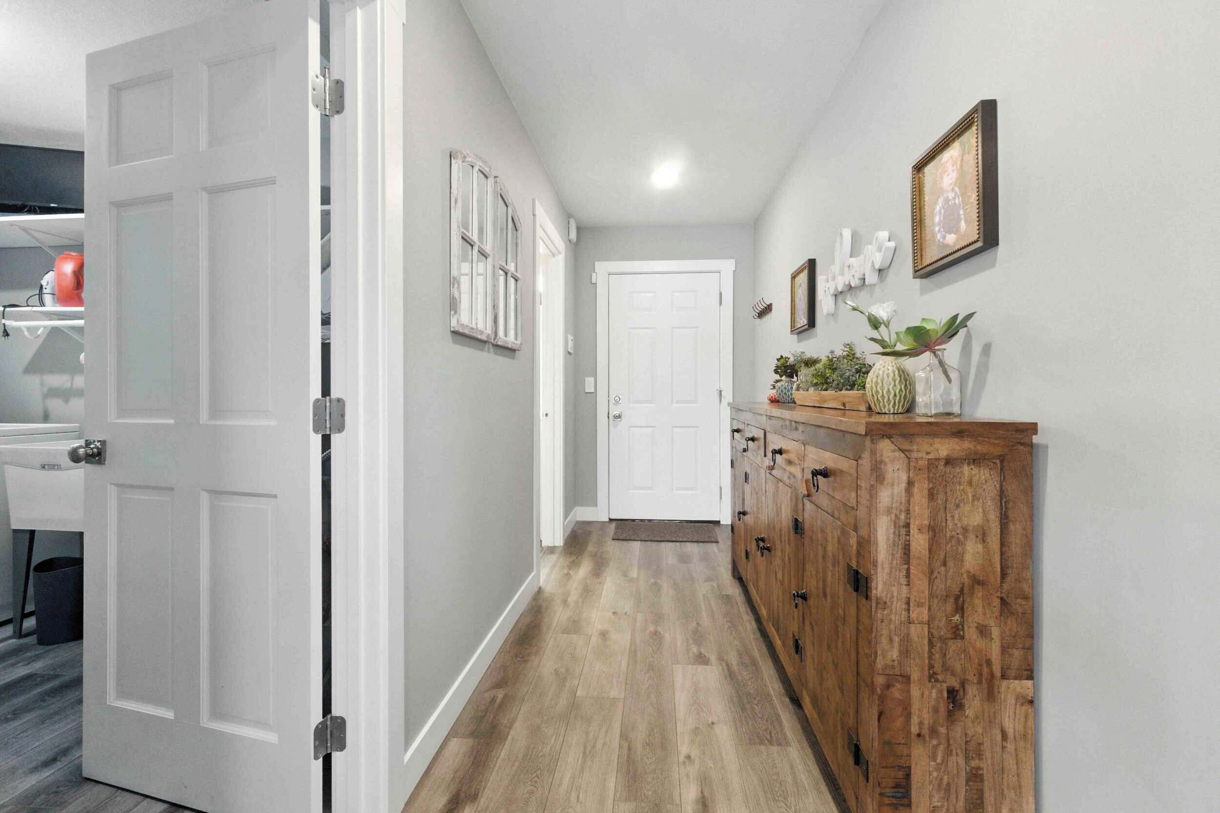 A hallway with a wooden floor, white walls, and a wooden cabinet with drawers.