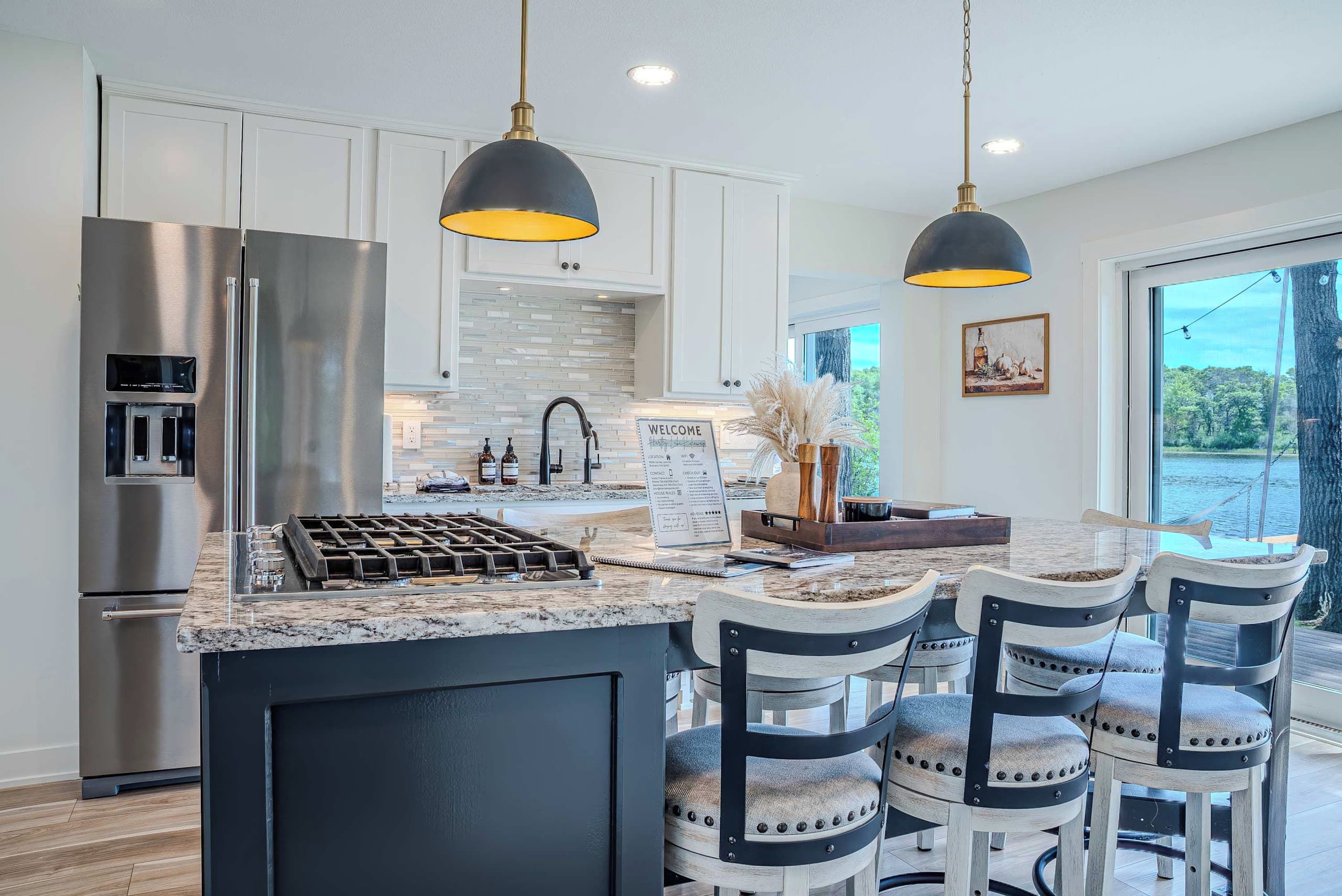 A modern kitchen with stainless steel appliances, a central island with bar stools, and pendant lighting.