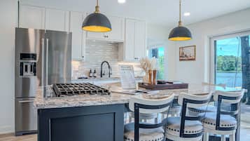 A modern kitchen with stainless steel appliances, a central island with bar stools, and pendant lighting.