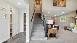 Una escalera conduce a un espacio de sala de estar con un sofá, una lámpara y un ventanal.