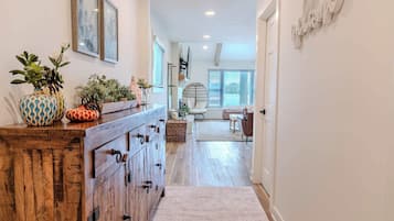 A hallway with a wooden cabinet, potted plants, and a rug leading to a dining area with a chair and table.