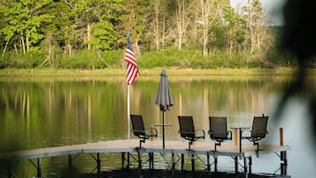 A lakeside dock with a flag, chairs, and tables.