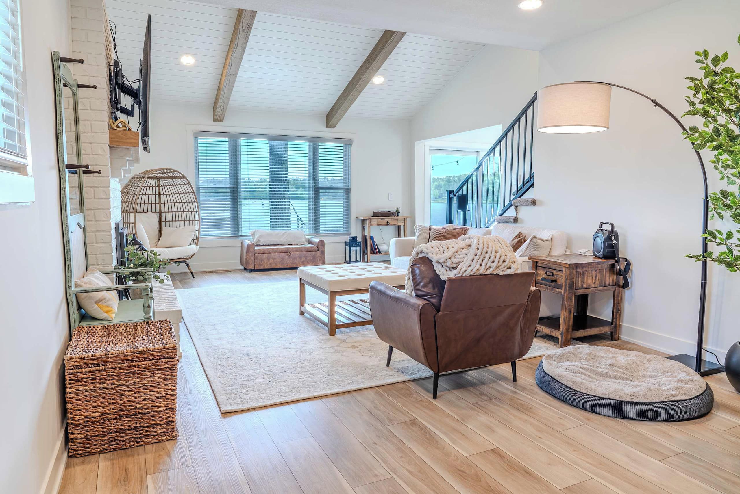 A spacious living room with a high ceiling, a staircase, and large windows.