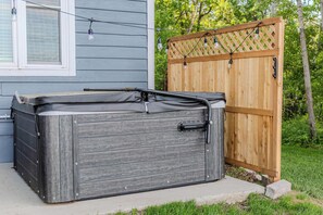 A hot tub with a wooden exterior, positioned next to a wooden fence and a house with siding.