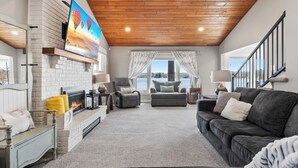 Amplia sala de estar con chimenea, asientos cómodos y un televisor grande montado en la pared.